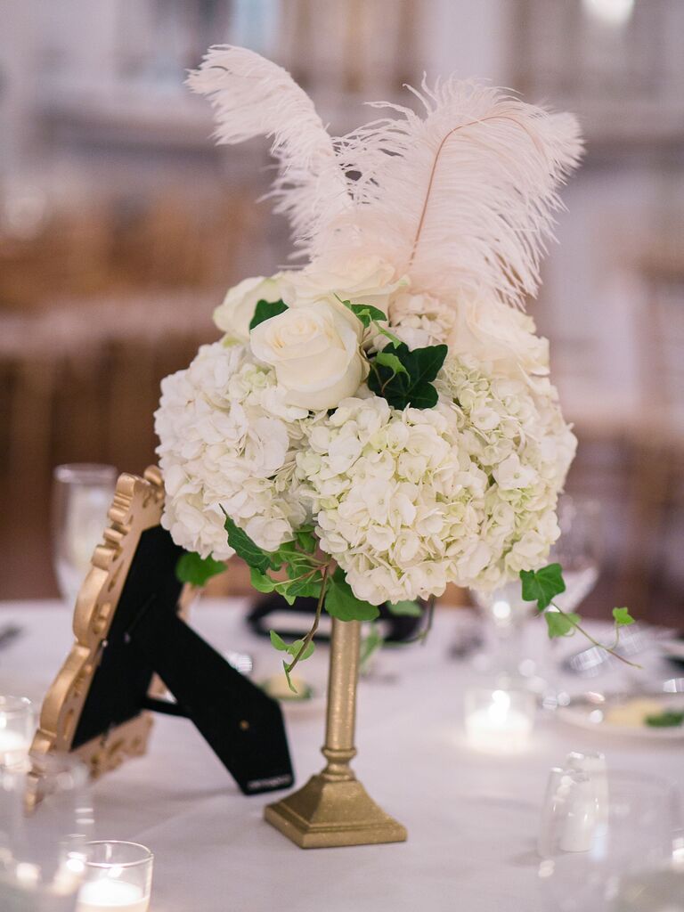 small NYE wedding centerpiece with white hydrangeas, roses and feathers in a low gold vase