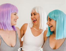 Three friends smile at one another while wearing multicolored wigs