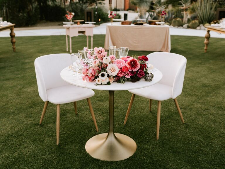 simple wedding sweetheart table with pink, white and red centerpiece and white velvet bucket chairs