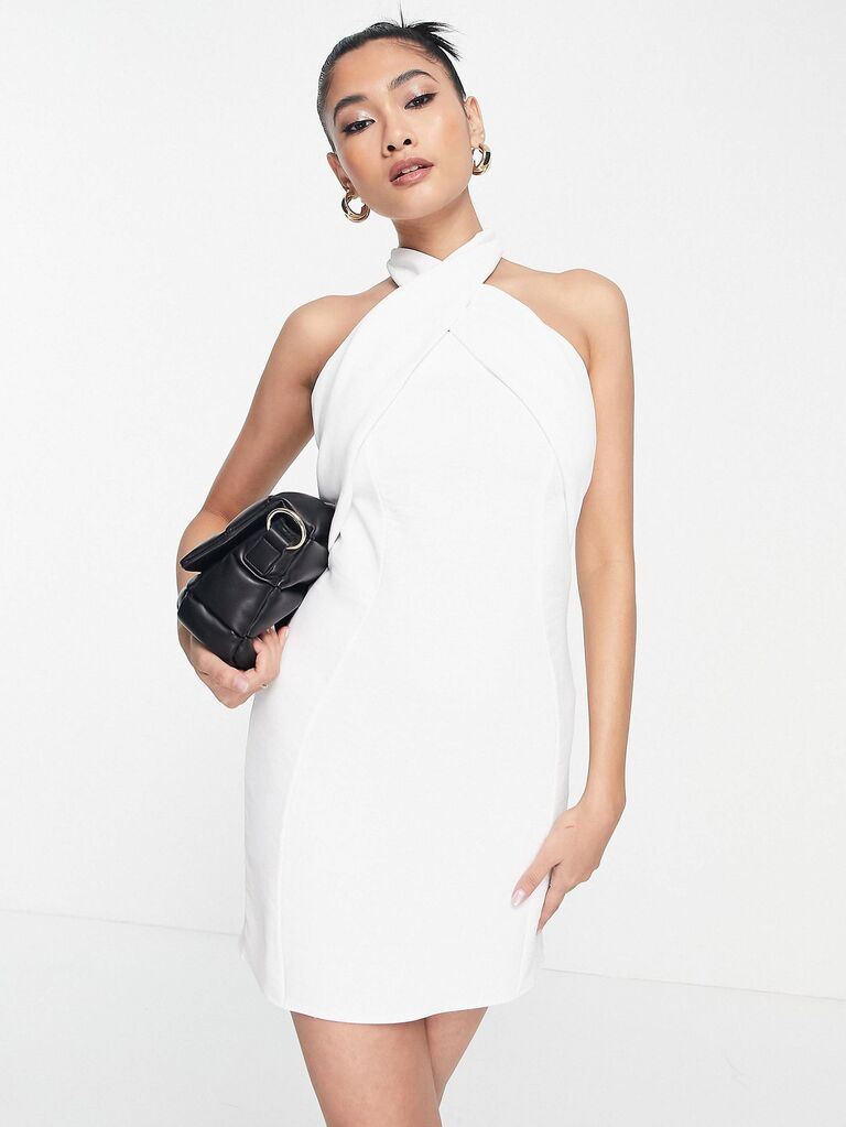 Model wears a short white dress with a halter neckline. 