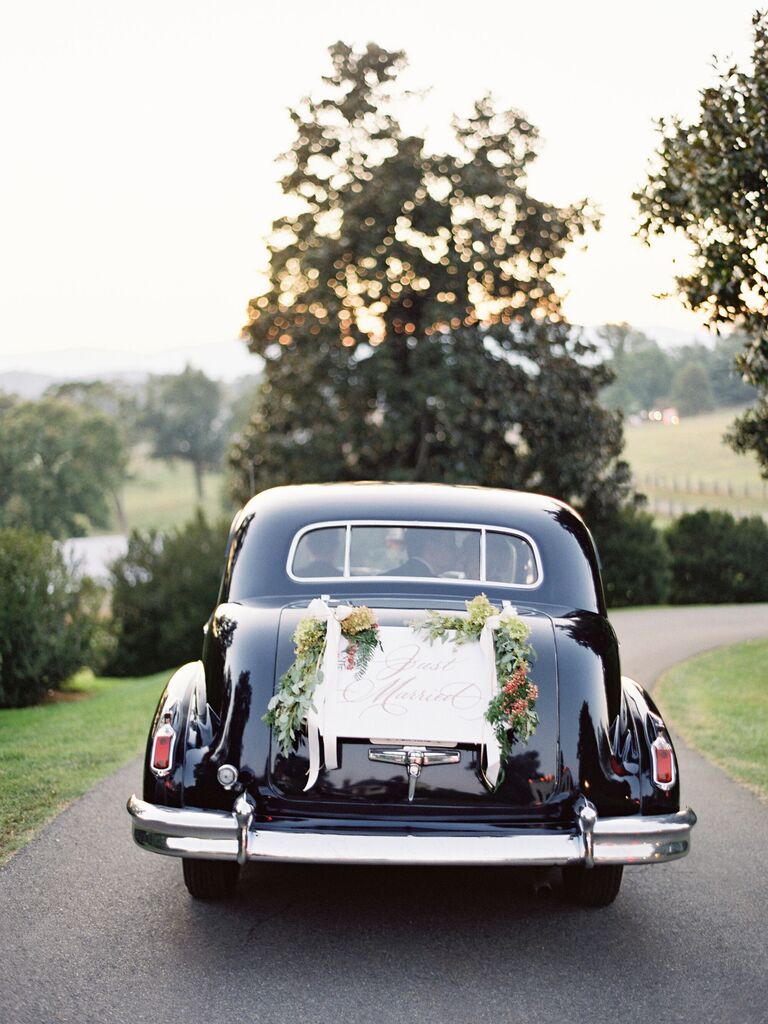 view of newlywed couple kissing through the back window of black vintage car decorated with 
