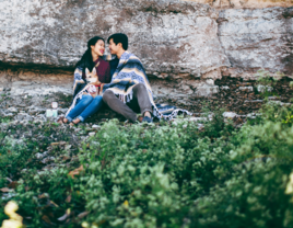 Couple sharing blanket and smiling at eachother on hillside in Texas