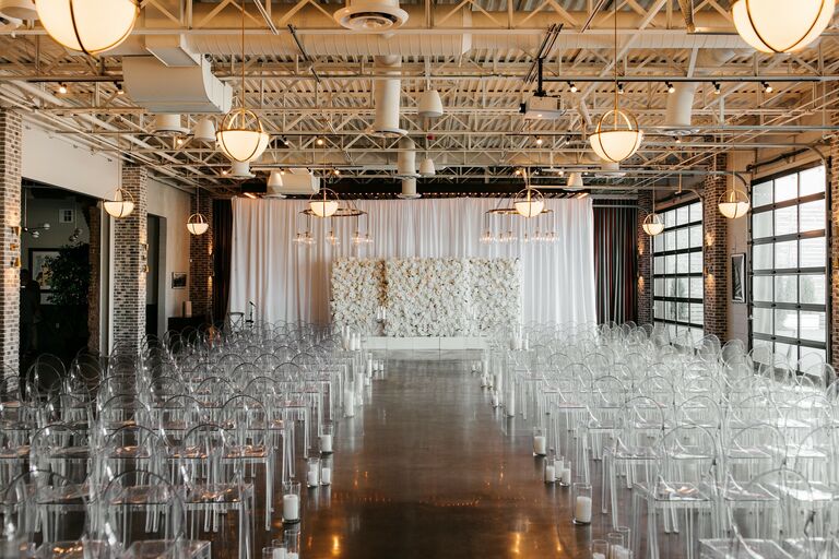 Wedding ceremony in loft with acrylic ghost chairs and white flower wall backdrop