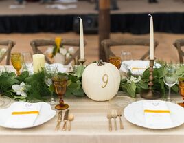 fall wedding tablescape with greenery table runner, white taper candles and white pumpkin table number with 9 in gold lettering