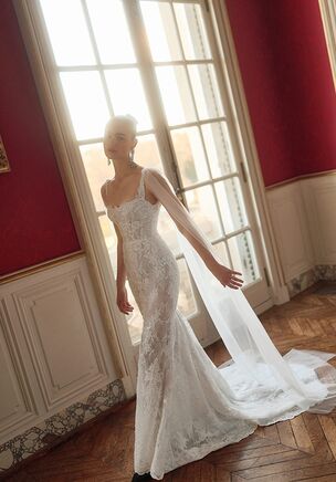 Orlando pairs Chantilly lace with delicate overlays in an ivory bridal gown. The hourglass base features a contoured sweetheart neckline, slender straps, and a chapel train. Exposed boning and corset details structure the beaded bodice. A matching ivory cape attaches at the shoulders, providing a convertible layer that reveals the open low-back design. This White collection gown by WONÃ Concept showcases tactile depth and fluid, trailing movement.