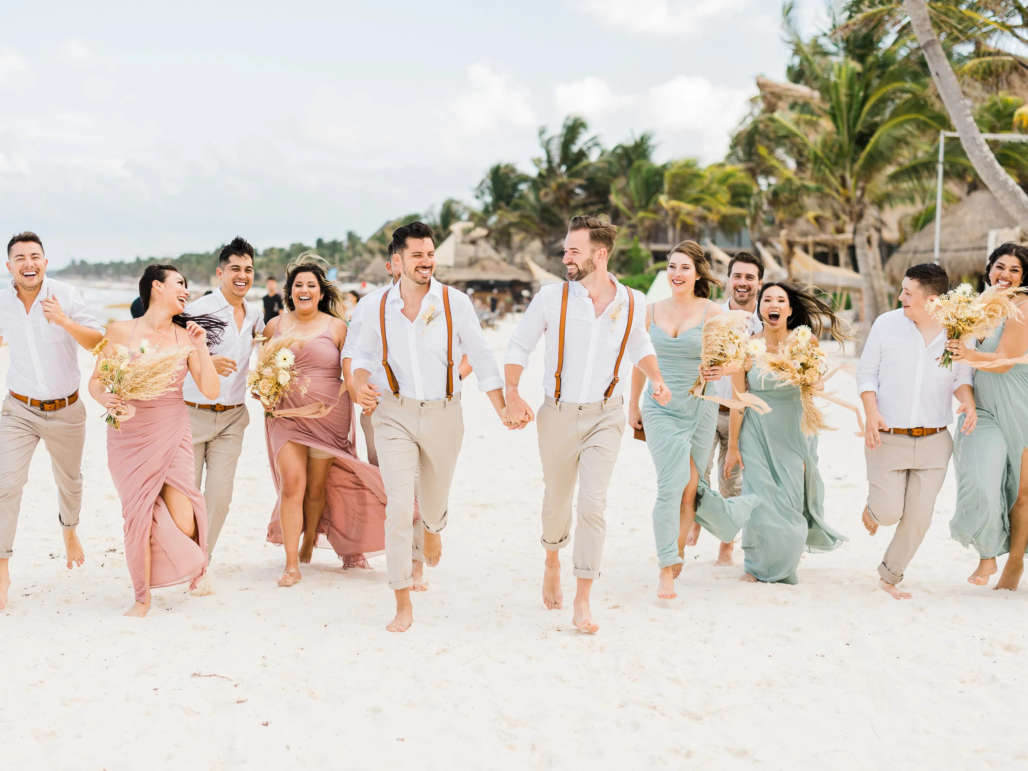 Grooms holding hands running with wedding party down the beach at Tulum destination wedding