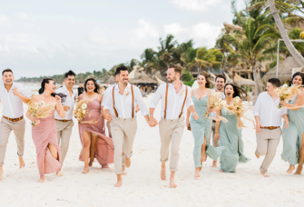 Grooms holding hands running with wedding party down the beach at Tulum destination wedding