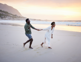 Couple holding hands walking on beach at engagement moon