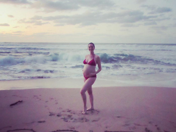 Anne Hathaway in a red bikini showing off her pregnant belly and smiling