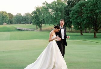 Happy couple walking hand in hand with a glass of champagne on a fairway