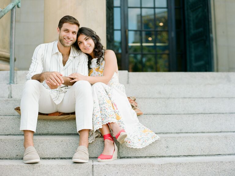 Couple poses for the camera while sitting on steps. 