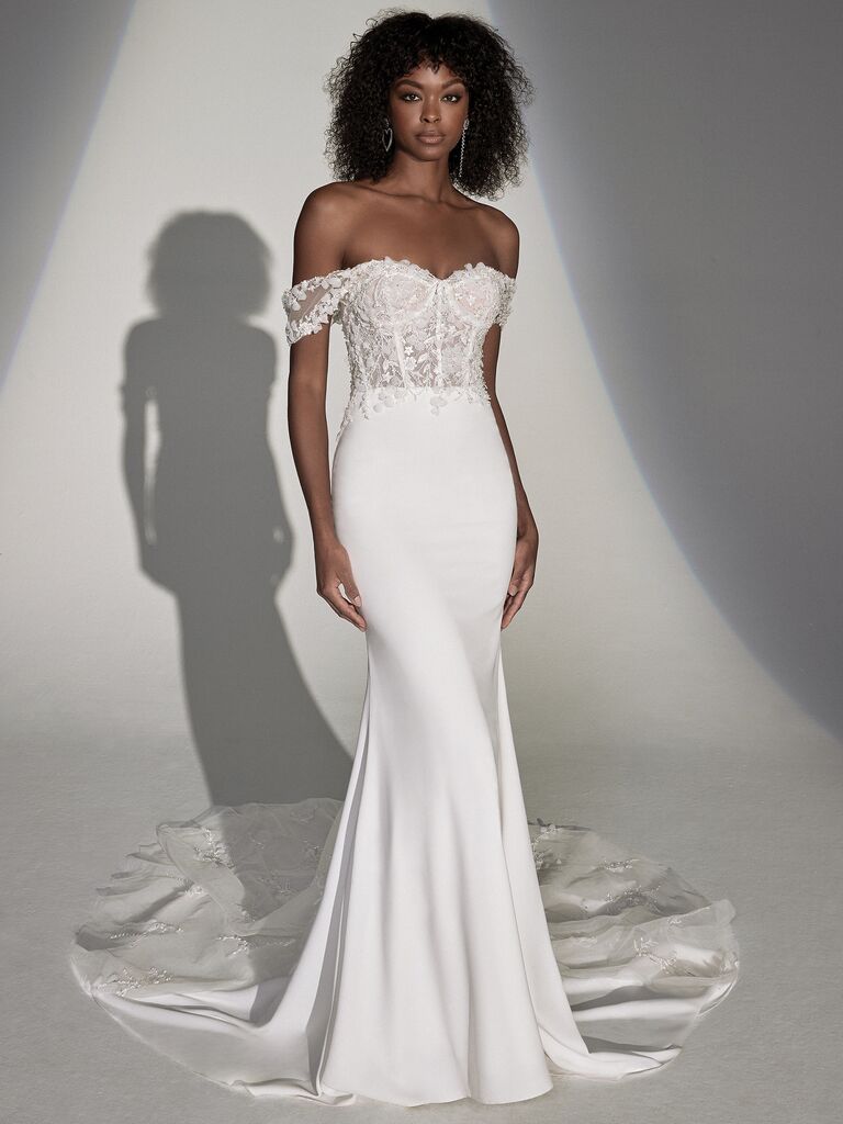 model stands against white backdrop wearing fit and flare crepe wedding dress with lace bustier bodice