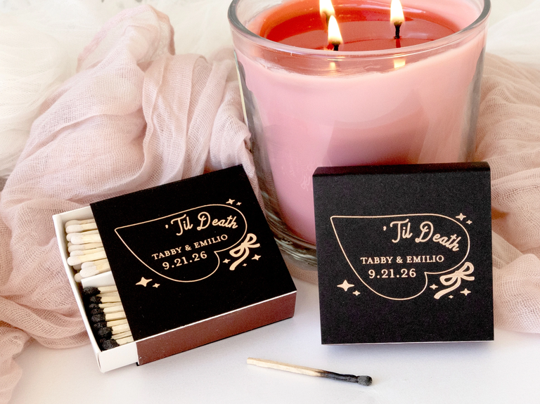 Extra-large, black matchboxes with a heart, bow and star motifs and the text "'Til Death" with a couples personalization for a wedding matchbook favor