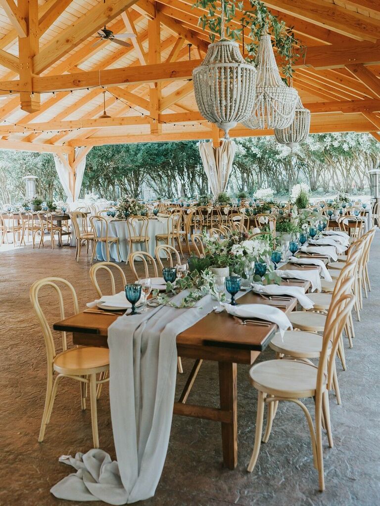 long wedding banquet table with light wooden bentwood cafe chairs underneath beaded boho chandelier