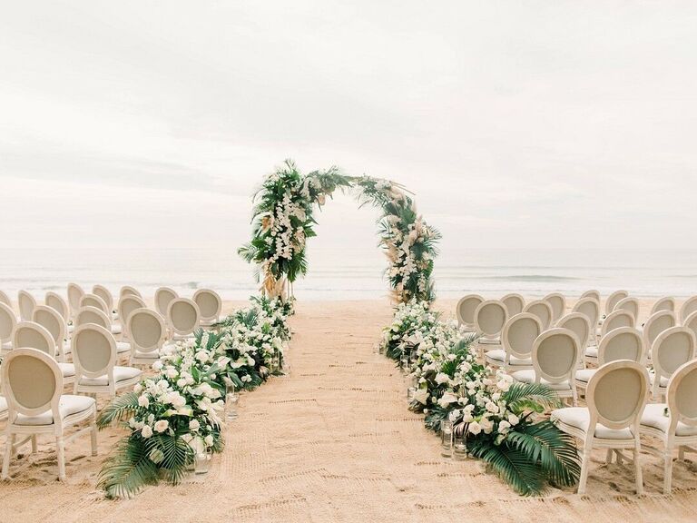 Romantic greenery arch and upholstered chairs on beach