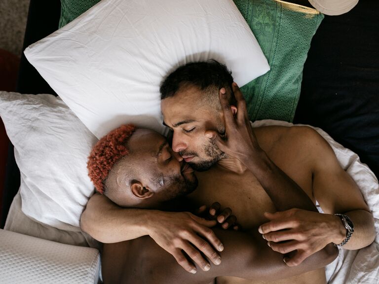 Two men cuddle together on a bed
