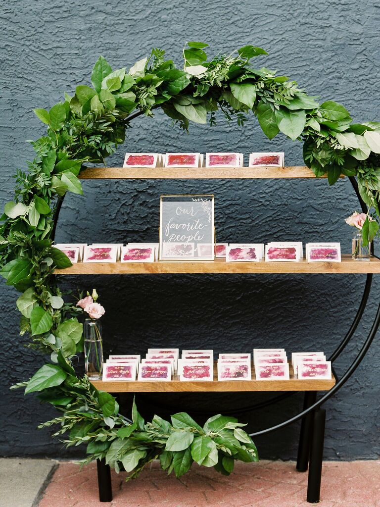 Escort card display with circular shelving unit covered in greenery