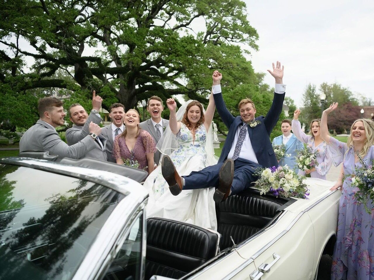 Happy couple celebrating in a convertable with wedding party