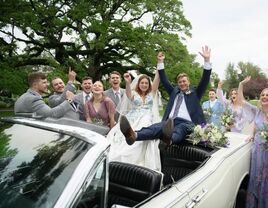 Happy couple celebrating in a convertable with wedding party