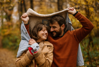 Couple bundling up under jacket together during fall 