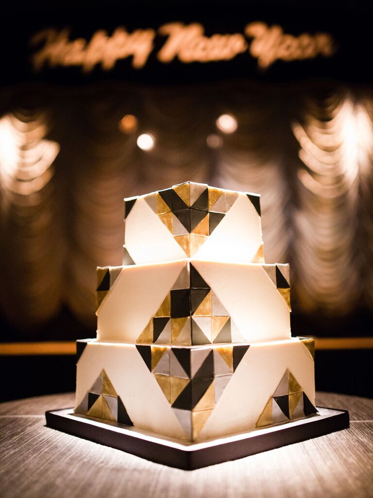 three tier square wedding cake decorated with white fondant and gold, silver and black triangle shapes