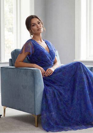 Romantic and effortlessly charming, this Heather Print Organza full A-line gown is a stunning choice for the Mother of the Bride. The V-neckline is delicately finished with tone-on-tone beading, complemented by flutter sleeves that create a soft, graceful silhouette. The natural waistline is highlighted with a sparkling beaded waistband for added elegance, and the flowing skirt moves beautifully with every step. This gown is whimsical, refined, and utterly unforgettable.