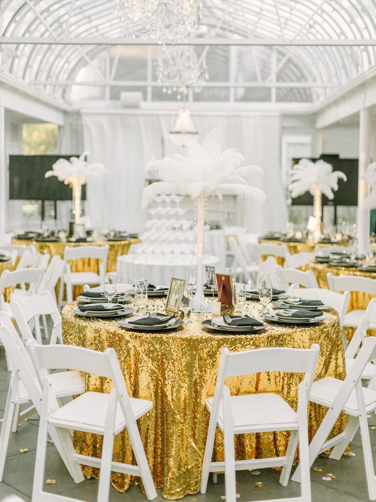 round wedding table decorated with gold sequin tablecloth and tall centerpiece of white feathers