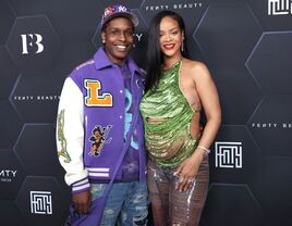 Singer Rihanna and boyfriend smile at the camera while walking a red carpet. 