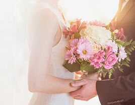 Bride holding a pink and white bridal bouquet, held in her father's hands