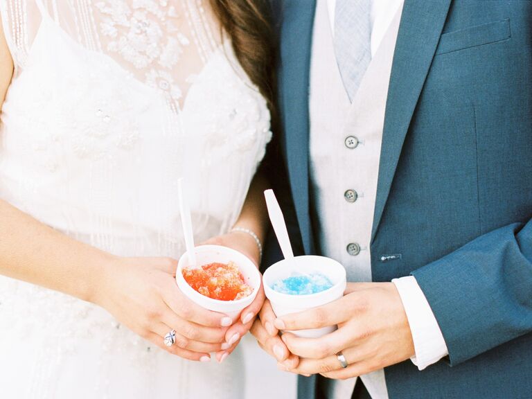Couple holds cups of colorful snow cones in hand. 
