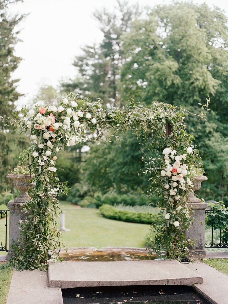 Ceremony arch in garden covered in greenery and white roses