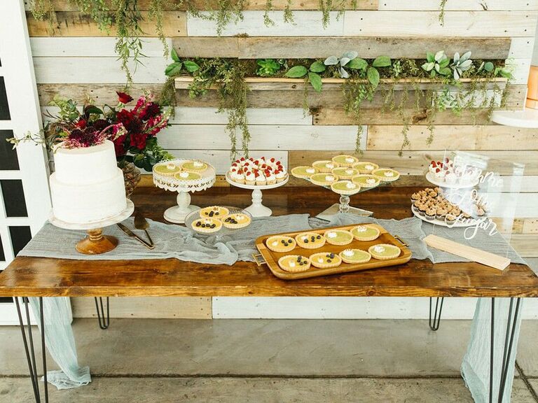 Rustic wood farmhouse dessert table with wedding cake, cupcakes and mini pies