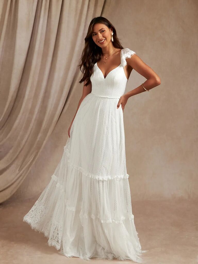 Model wears a romantic white gown with flutter sleeves. 