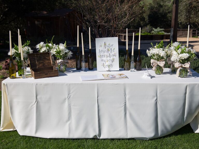 wedding gift table with white tablecloth, watercolor welcome sign, white flowers and white taper candles in wine bottles