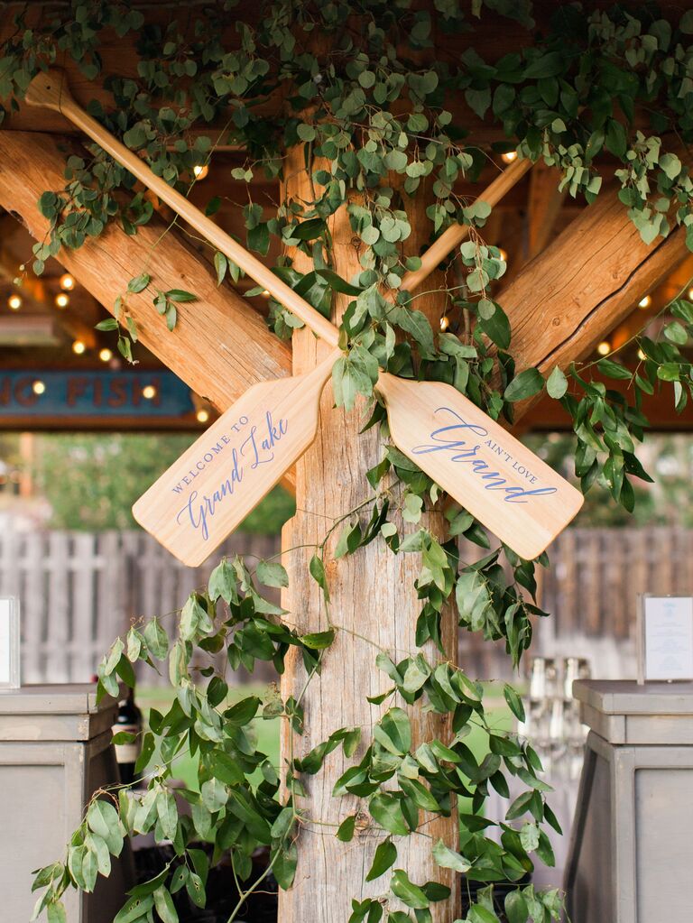 wedding welcome sign made from crossed wooden rowboat oars and decorated with greenery vines
