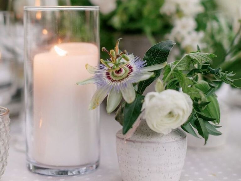 A bud vase with ranunculus and passionflower blooms beside pillar candle