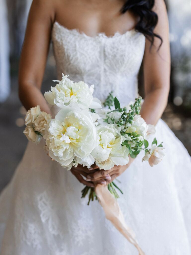 A bride holds a vibrant white peony bouquet.
